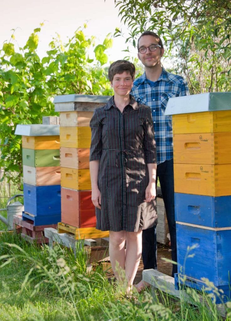 Frau und Mann stehen zwischen Bienenbeuten